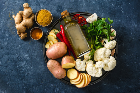 Raw ingredients cooking aloo gobi Indian food on dark stoneの写真素材