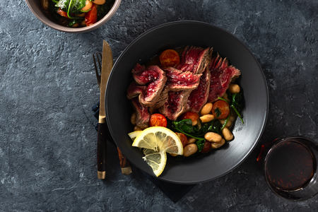 Dinner table. Beef steak with white beans, spinach and tomatoes on dark stone  top view with free copy spaceの写真素材