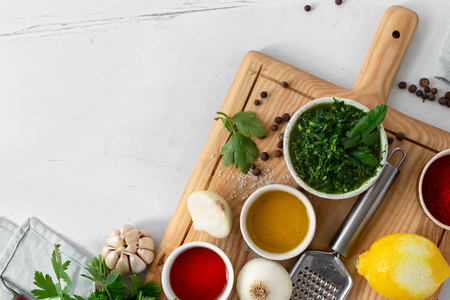 Raw ingredients for cooking Argentinian green Chimichurri or Chimmichurri salsa or sauce on white wooden table with copy spaceの写真素材