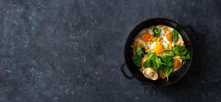 Healthy breakfast table with fry pan eggs with spinach and corn on dark stone  top viewの写真素材