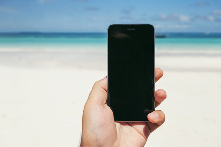 Hands holding phone with empty screen against the blue sky and ocean. Buying a tour online conceptの写真素材