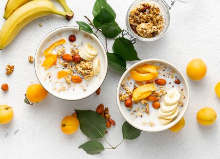 Granola cereal with fruits, nuts, milk and peanut butter in bowl on a white background. Healthy breakfast cereal top viewの写真素材