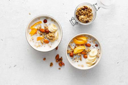Granola bowl with fruits, nuts, milk and peanut butter in bowl on a white background. Healthy breakfast cereal top viewの写真素材