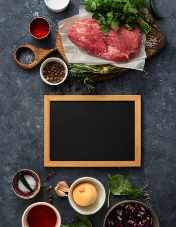 Cooking table with blank chalk board and beef meat, vegetables, spices, herbs top view. Food menuの写真素材
