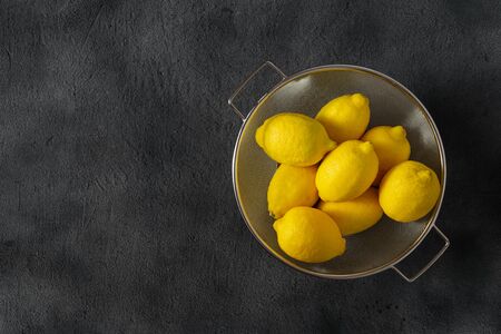 Pile of lemons in colander on a dark background with copy space top viewの写真素材