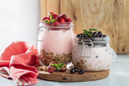 Granola yogurt with homemade strawberry and blueberry in glass jar on wooden board in home kitchenの写真素材
