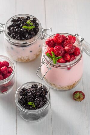 Healthy breakfast cereal with homemade strawberry, blueberry, blackberry and raspberry in glass jar on wooden board in home kitchenの写真素材