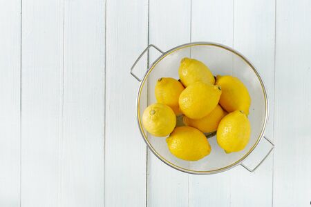 Pile of lemons in colander on a wooden table with copy space top viewの写真素材