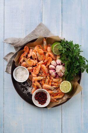 Raw prawns in a cooking pan with ingredients for preparation fried shrimps on blue wooden background top viewの写真素材