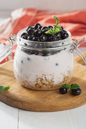 Granola yogurt in glass jar on a wooden board in home kitchenの写真素材