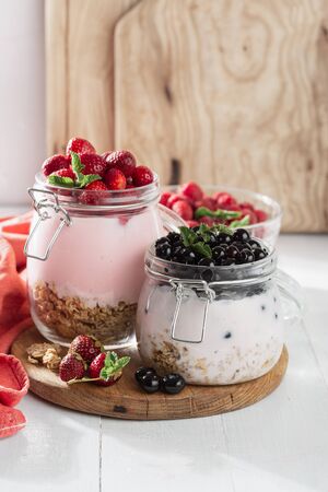 Healthy breakfast cereal with homemade strawberry and blueberry in glass jar on wooden board in home kitchenの写真素材