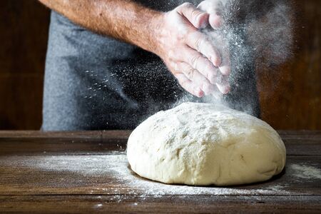 Man preparing bread dough on wooden table in a bakeryの写真素材
