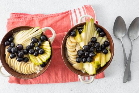 Plate with oatmeal and pear, apple, blueberry, banana on a white background top view. Breakfast table conceptの写真素材