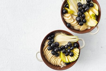 Plate with oatmeal and pear, apple, blueberry, banana on a white background top view with copy space. Sweet tasty and healthy breakfast table conceptの写真素材
