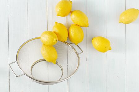 Pile of lemons in colander on a wooden table top viewの写真素材