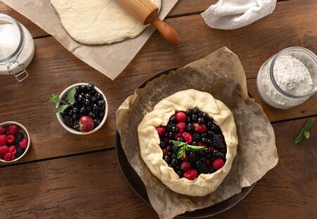 Raw fruits pie on a wooden table top view. Ingredients for cooking tart pie with biscuits, strawberry, blueberry, blackberry and raspberryの写真素材