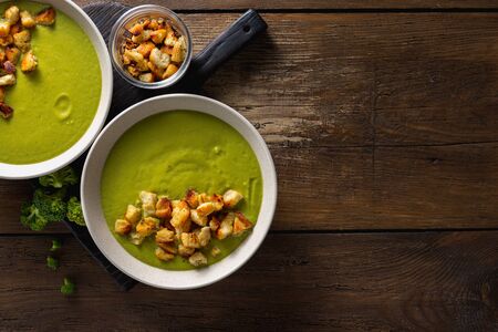 Bowl of cream broccoli soup with bread croutons on a woodenの写真素材
