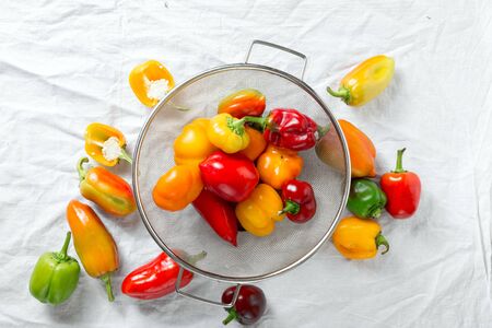 Washed yellow, red and green bell peppers in sieve on white background top viewの写真素材