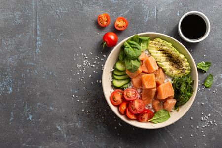 Organic poke bowl with salmon, avocado and vegetables on dark backgroundの写真素材