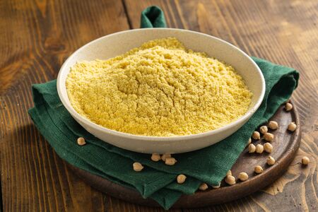 Chickpea flour in white ceramic bowl on wooden table with spilled chickpeasの写真素材