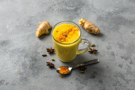 Indian drink turmeric golden milk in glass. Golden latte on light background with ingredients for cookingの写真素材
