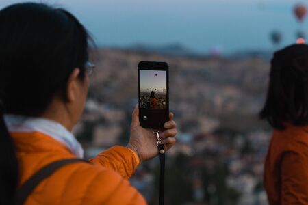 Woman taking a picture of a beautiful girlfriends with her smartphone against the Background of balloons in Cappadocia, Turkeyの写真素材