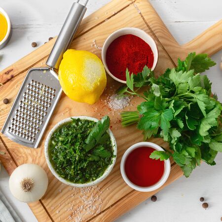 Top view cooking background. Raw ingredients for cooking green Chimichurri or Chimmichurri salsa or sauce on white wooden tableの写真素材