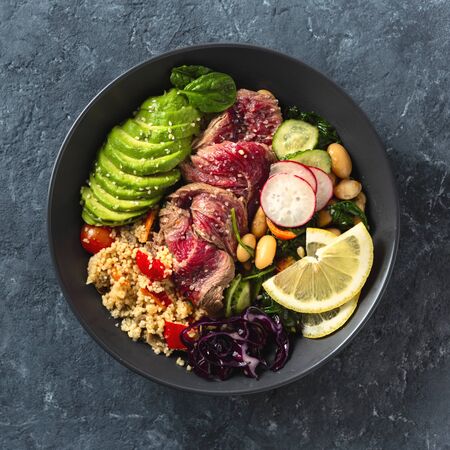 Healthy food buddha bowl with beef steak, beans, couscous, avocado and vegetables on dark background with copy spaceの写真素材