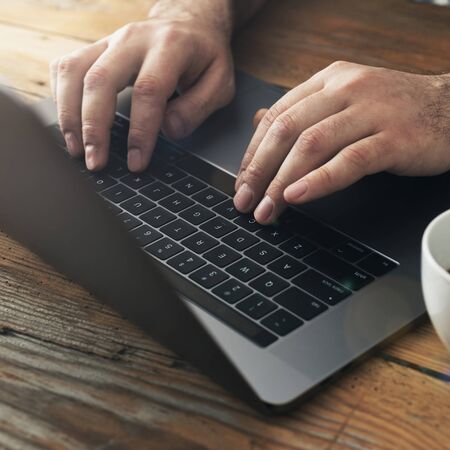 Man using laptop in home office. Male hands typing on keyboardの写真素材