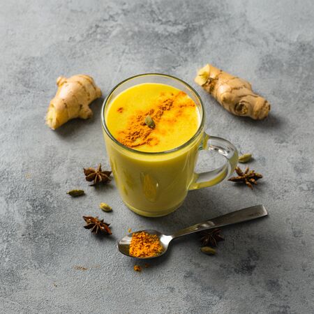 Indian drink turmeric golden milk in glass. Golden latte on light background with ingredients for cookingの写真素材