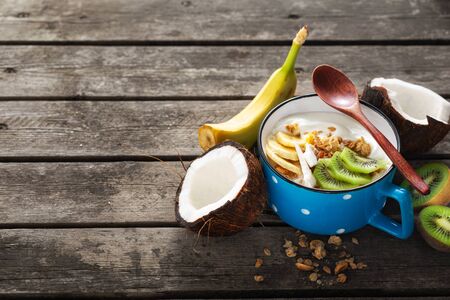 Coconut yogurt fruits with granola served on wooden table. Copy space. Probiotic food concept. Tasty and healthy breakfastの写真素材