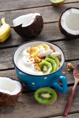 Tasty and healthy breakfast. Bowl fruit coconut yogurt with granola on wooden table. Healthy vegan food conceptの写真素材