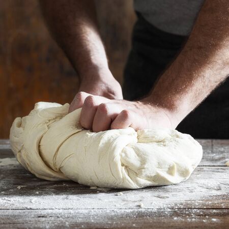 Man kneads bread dough on wooden table in a bakery close upの写真素材