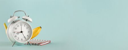 Old alarm clock with banana and notepad on light background with copy space. Education conceptの写真素材