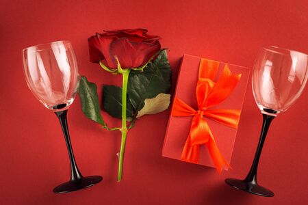 Valentine's day or mother's day concept. Red gift box with flowers rose and wine glasses on red background top viewの写真素材
