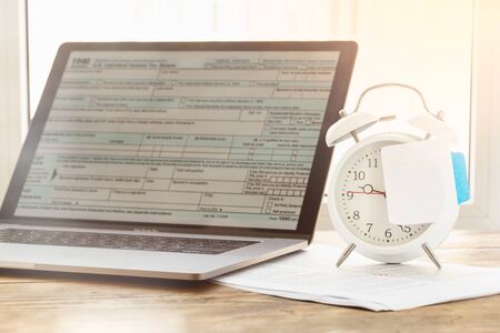 Tax planning. Laptop with form individual income tax returns  on alarm clockの写真素材