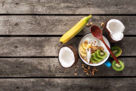 Tasty and healthy breakfast. Bowl fruit coconut yogurt with granola on wooden table Copy space Top view Healthy vegan food conceptの写真素材