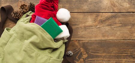 Backpack with passport, santa claus hat and Christmas festival decorations on wooden background. Copy space. Holiday travel backgroundの写真素材