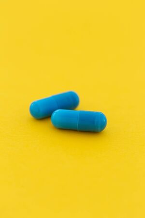 Pharmaceutical medicine blue capsule pills on a yellow backgroundの写真素材