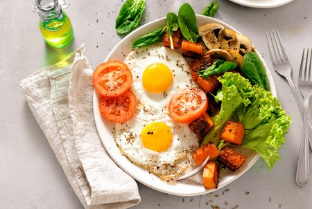 Top view breakfast table. Breakfast plate with fried eggs, vegetables, mushrooms and toast on gray concreteの写真素材