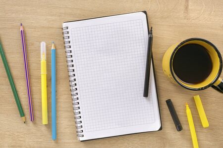 Office desk with epmty notebook, cup coffee, colored markers and pencils top viewの写真素材