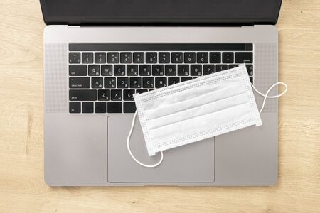 Coronavirus Working from home concept Laptop with protective mask on wooden table top view