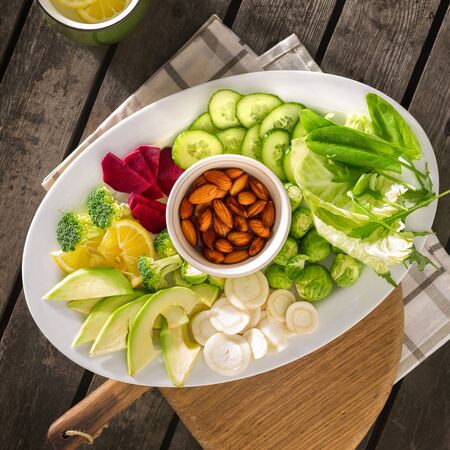 Plate of fresh healthy vegetarian food. Various vegetables and nuts in plate on wooden table top viewの写真素材