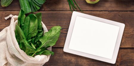 Order food online Tablet with blank screen on wooden background with fresh green vegetables and...