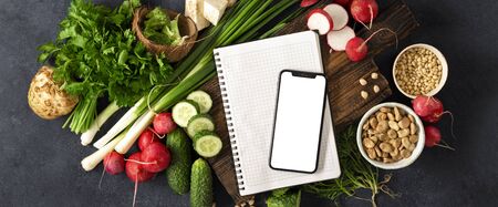 Smartphone with blank screen and notepad with ingredients for cooking vegan food.の写真素材