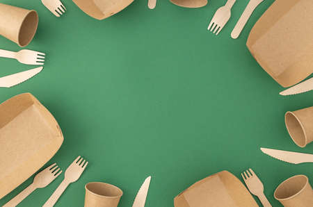 Frame of disposable paper cups and plate with wooden forks and knives on green background. Pattern zero waste, plastic free conceptの写真素材