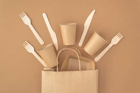 Zero waste, plastic free concept. Paper bag with disposable paper cups, plate, wooden forks and knives on beige background. Eco sustainable livingの写真素材