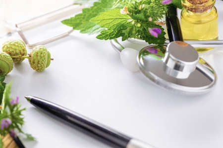 Alternative medicine. Clipboard with stethoscope, various plants, leaves of healing herbs and healthy oils close upの写真素材