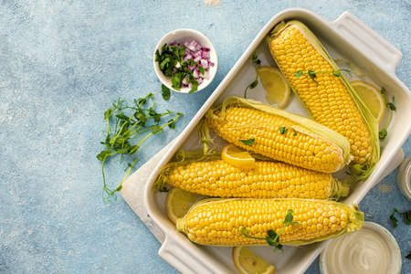 Raw cob corn in baking dish with ingredients for preparing healthy vegetarian food top viewの写真素材
