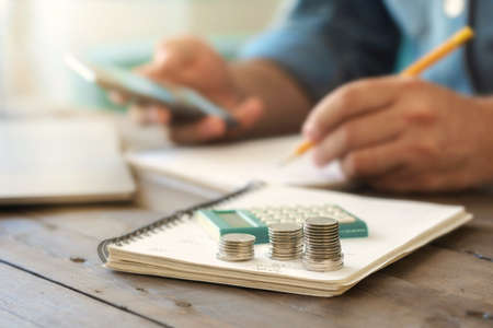 Stacks of coins on a wooden table with a calculator. Taxing, home accounting or credit analysis for mortgage payment conceptの写真素材